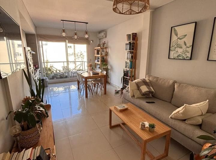 Living comedor amueblado con sillón, mesa ratona y estanterías, con balcón al fondo.