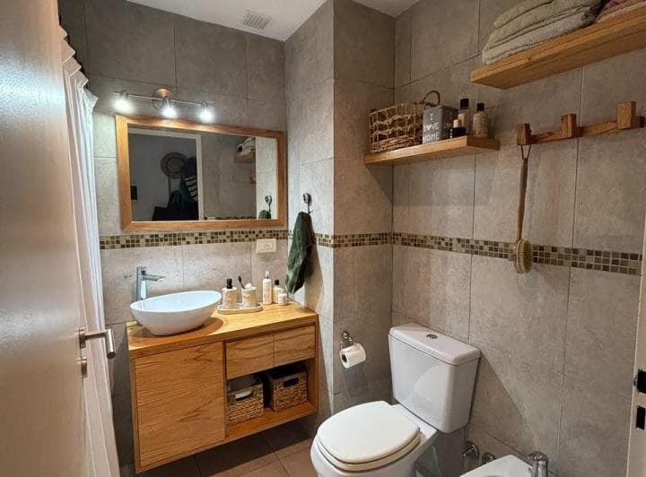 Baño moderno con inodoro, bidet y vanitory de madera con bacha blanca.