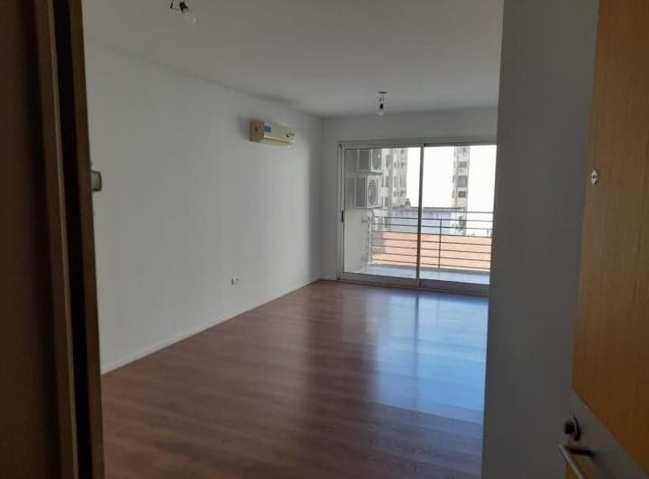 Living vacío con piso flotante, aire acondicionado y acceso a balcón.
