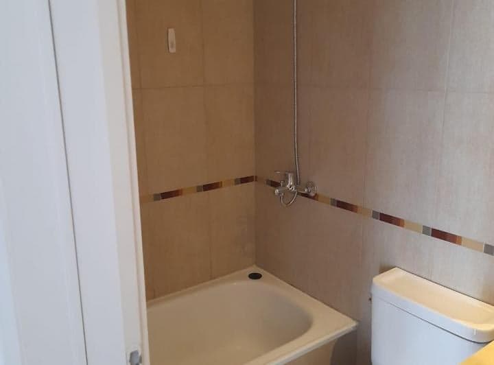 Baño con bañera, ducha y azulejos marrones claros.