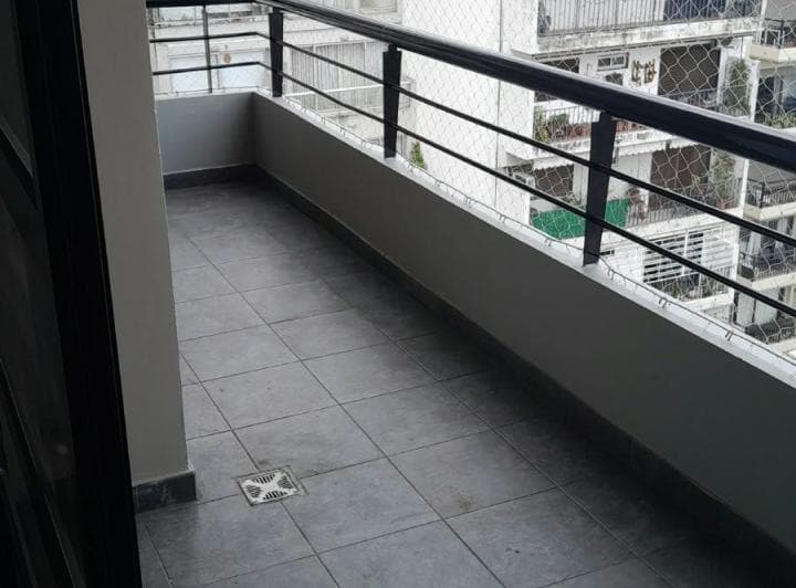 Balcón amplio con piso de baldosas y baranda, vista a otros edificios.