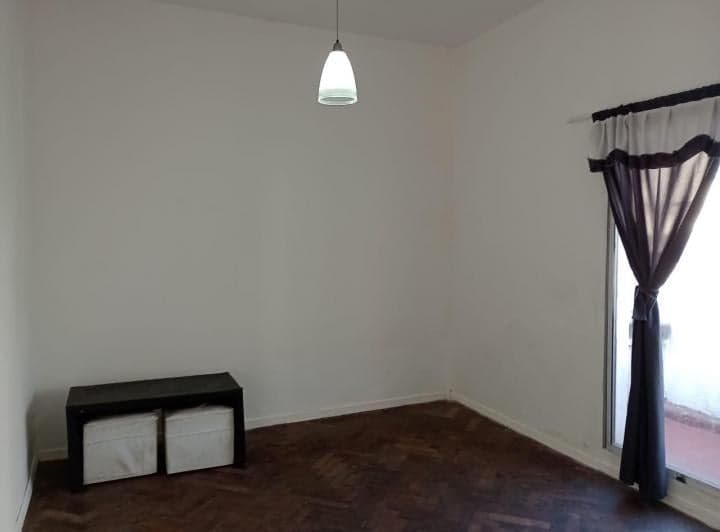 Living vacío con piso de parquet, ventana y pequeño banco