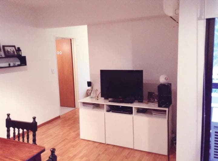 Living con televisión, mueble blanco y puerta a otra habitación.