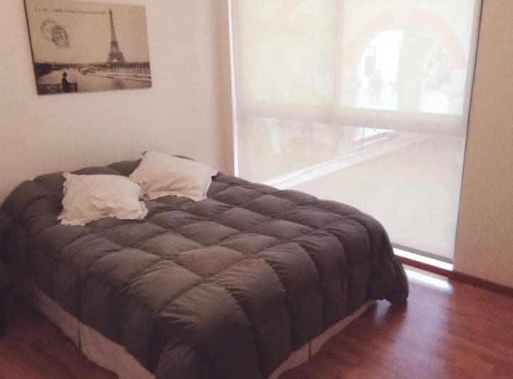 Dormitorio con cama de dos plazas, cubrecama gris y ventana.
