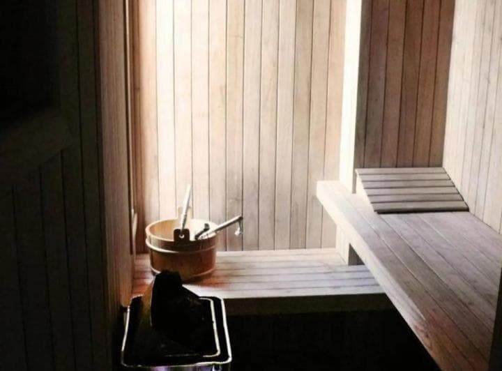 Sauna de madera con banco, cubo de agua y calentador.