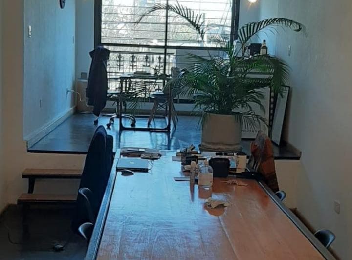 Living con mesa de trabajo, ventana con rejas y planta.