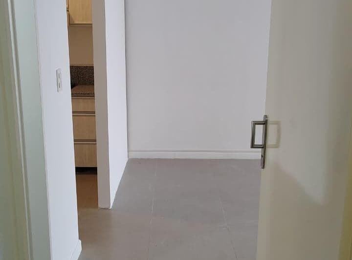Living vacío con puerta abierta y vista parcial a una cocina.