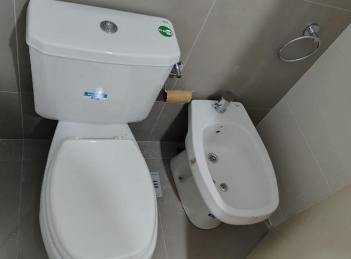 Inodoro y bidet blancos en baño con azulejos grises.