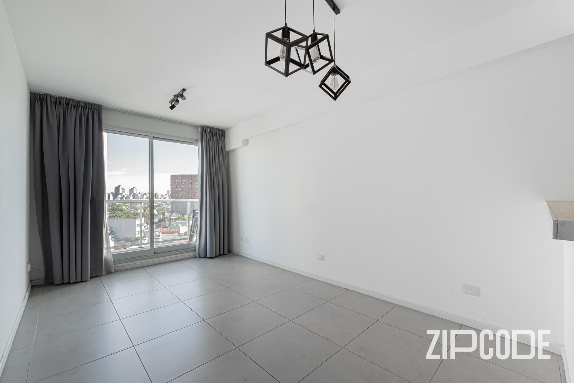 Living comedor vacío con ventana, cortinas grises y luminaria colgante.
