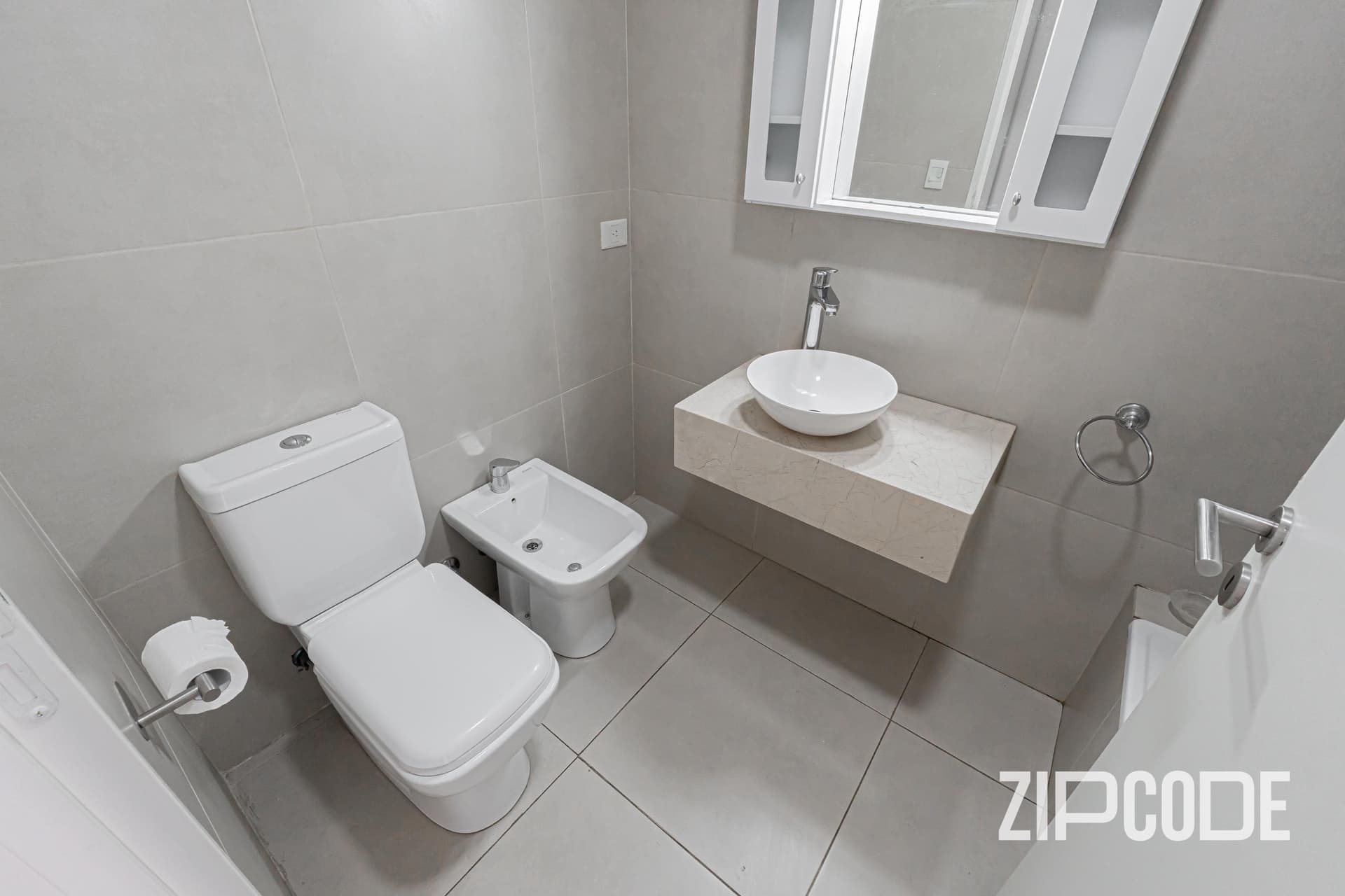 Baño con inodoro, bidet, lavatorio de bacha y botiquín con espejo.