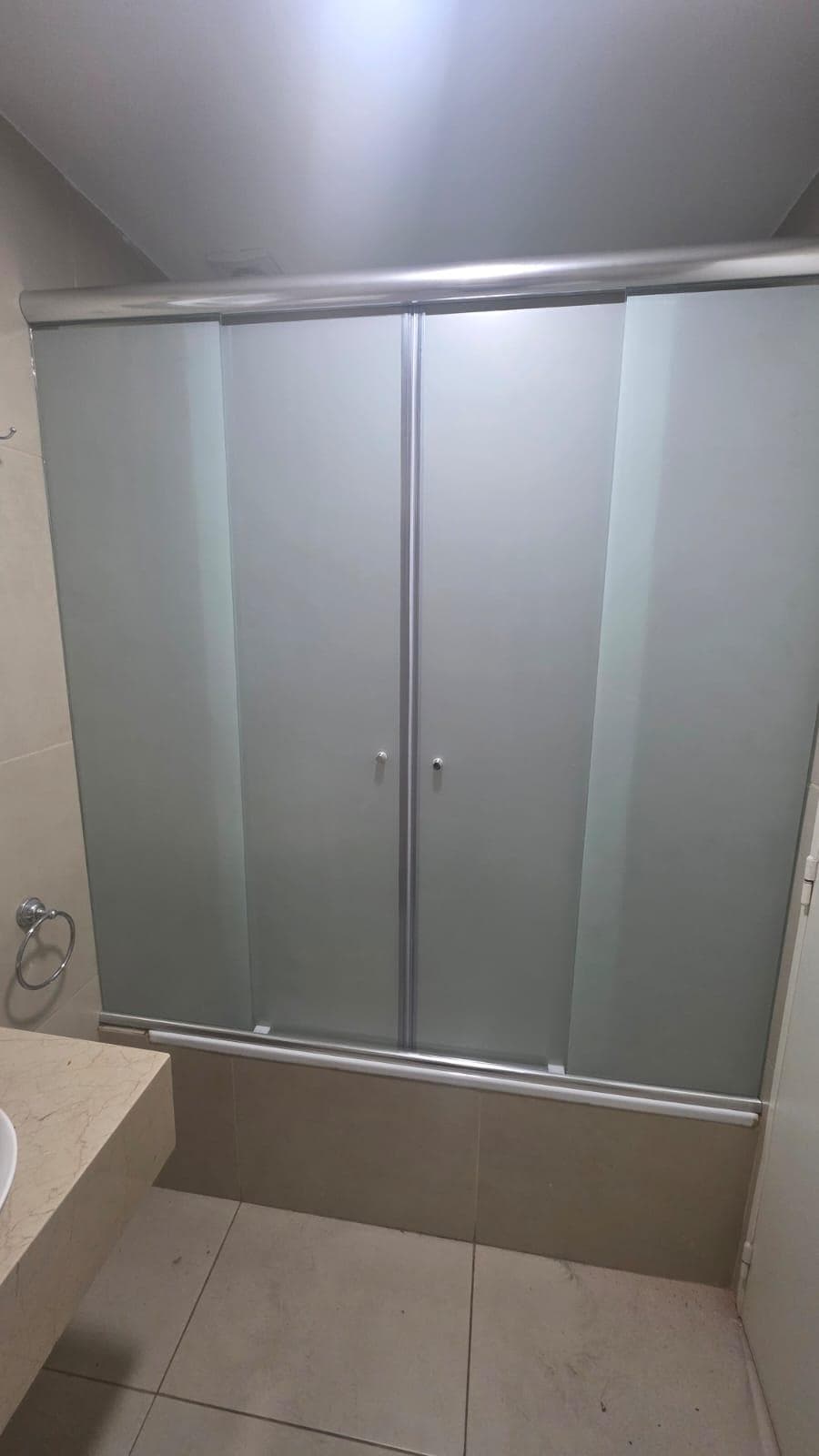 Ducha con mampara esmerilada, mesada de mármol y azulejos claros.