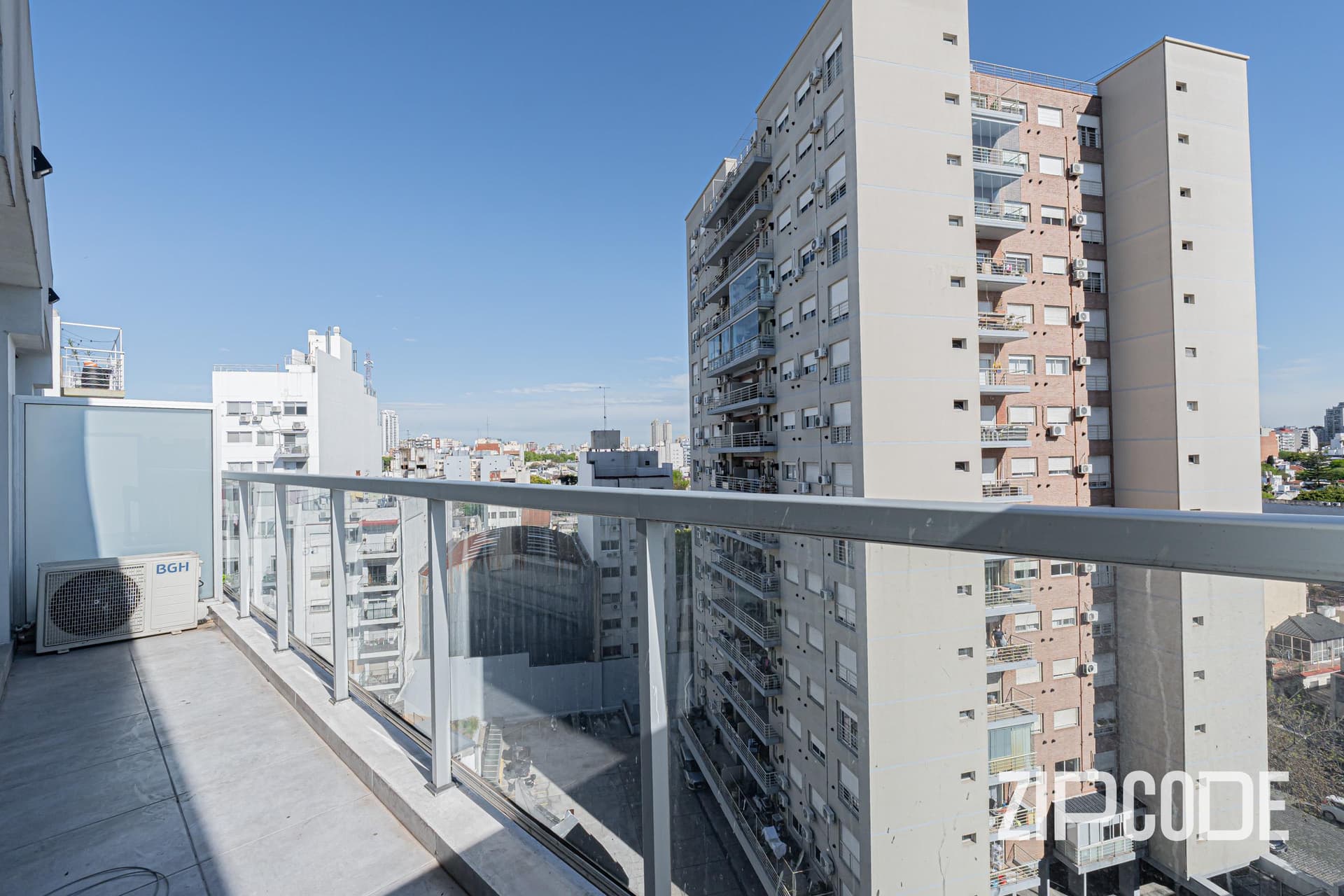 Balcón con baranda de vidrio, vista a edificios y ciudad.