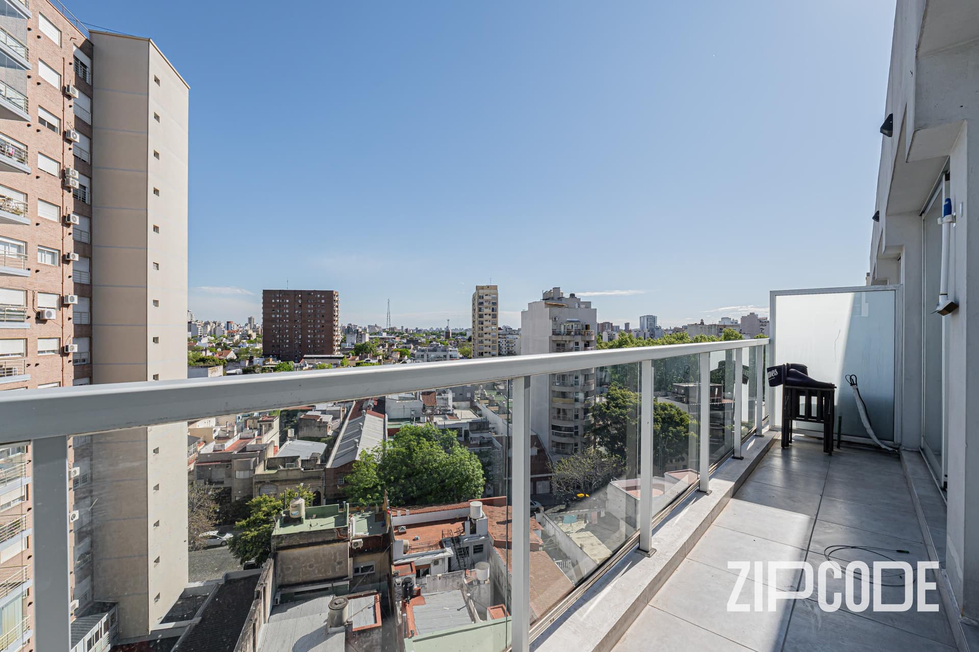 Balcón amplio con baranda de vidrio y vista panorámica a la ciudad.