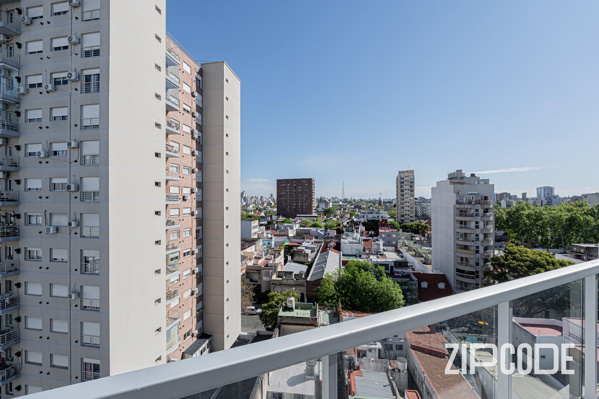 Balcón con baranda de vidrio, vista a edificios y horizonte de la ciudad.