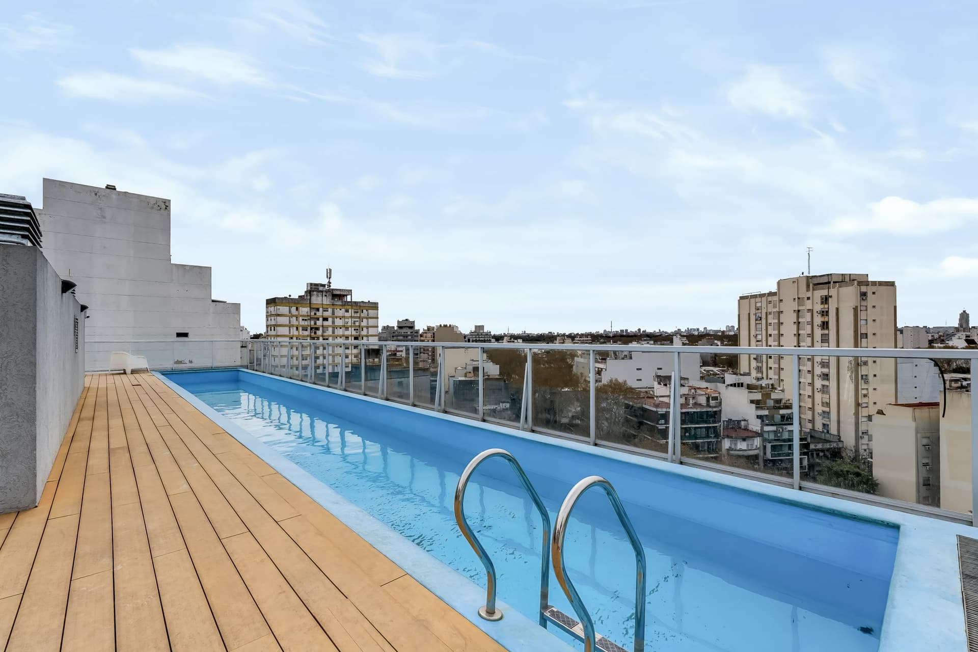 Pileta de natación en azotea con deck de madera y baranda de vidrio.