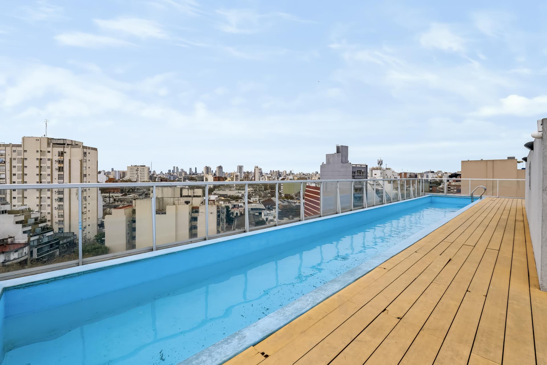 Pileta larga en azotea, con vista a la ciudad y deck de madera.