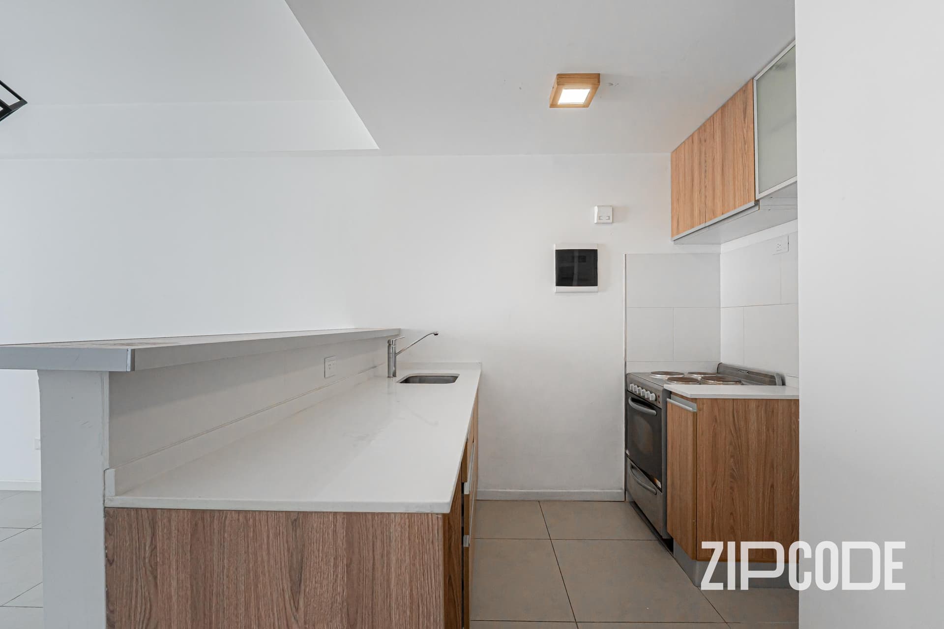 Cocina integrada con barra, mesada, anafe y alacenas de madera.