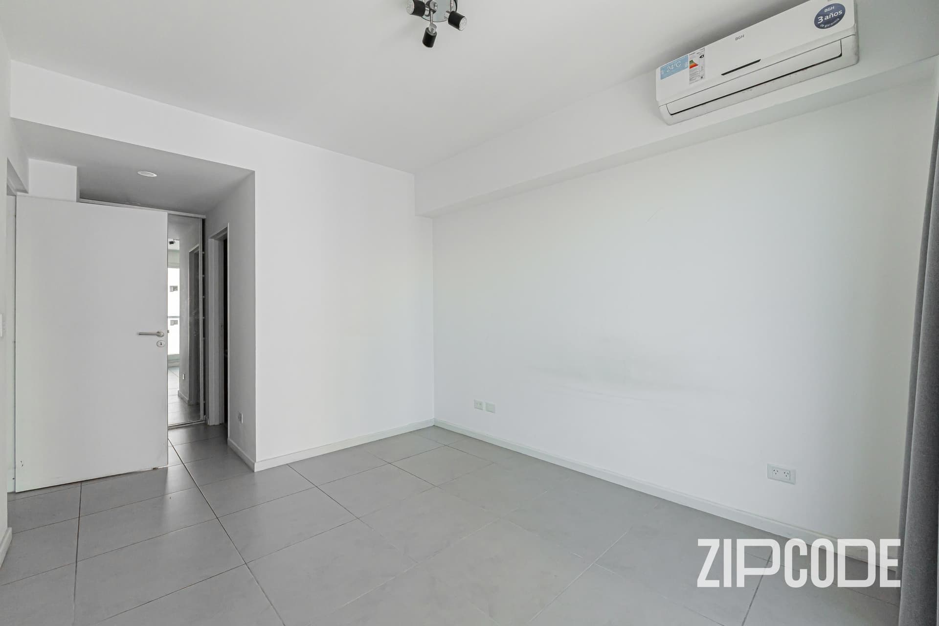 Dormitorio vacío con aire acondicionado, puerta y pasillo de entrada.
