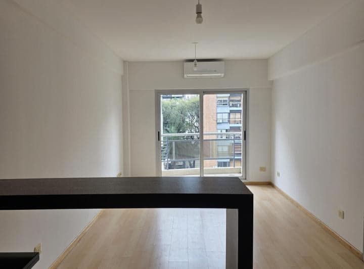 Living comedor vacío con balcón, aire acondicionado y piso de madera.