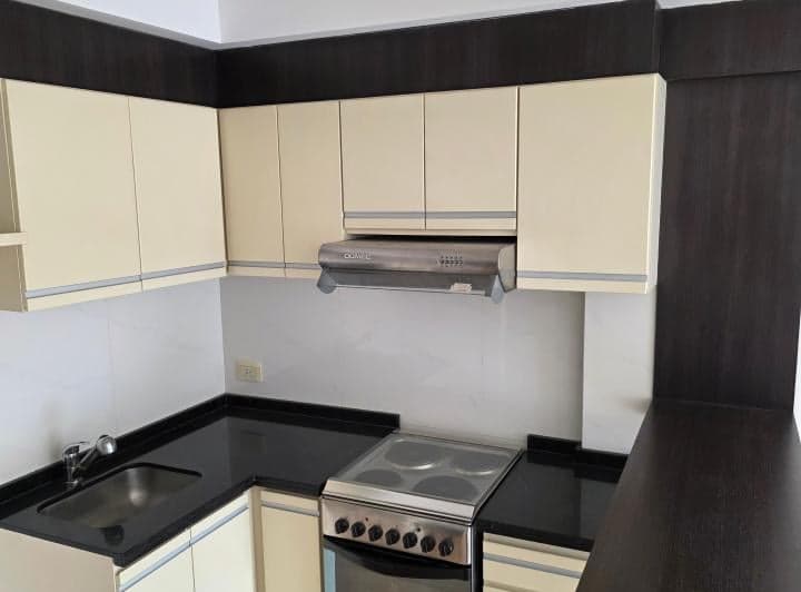 Cocina con mesada negra, anafe eléctrico, bacha y campana extractora.