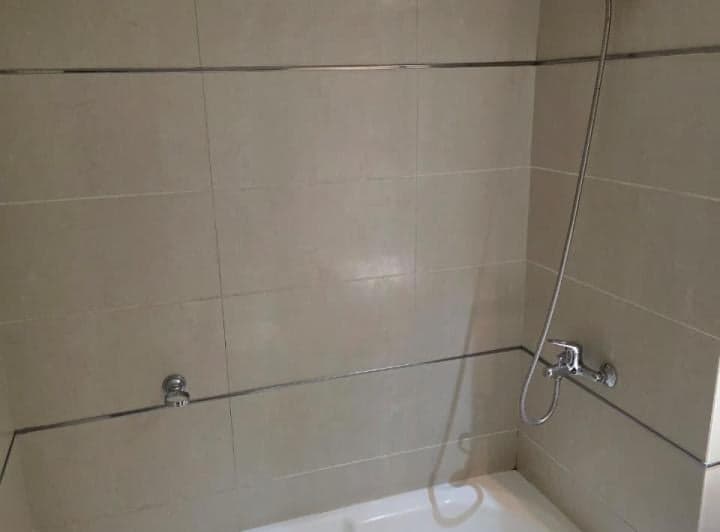 Ducha con bañera, grifería y azulejos beige en el baño.