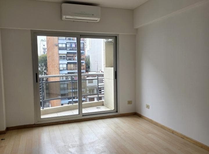 Dormitorio vacío con ventanal al balcón y aire acondicionado split.