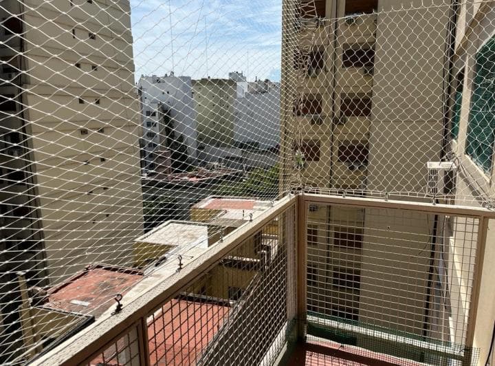 Balcón con rejas de seguridad y vista a edificios vecinos bajo cielo parcialmente nublado.