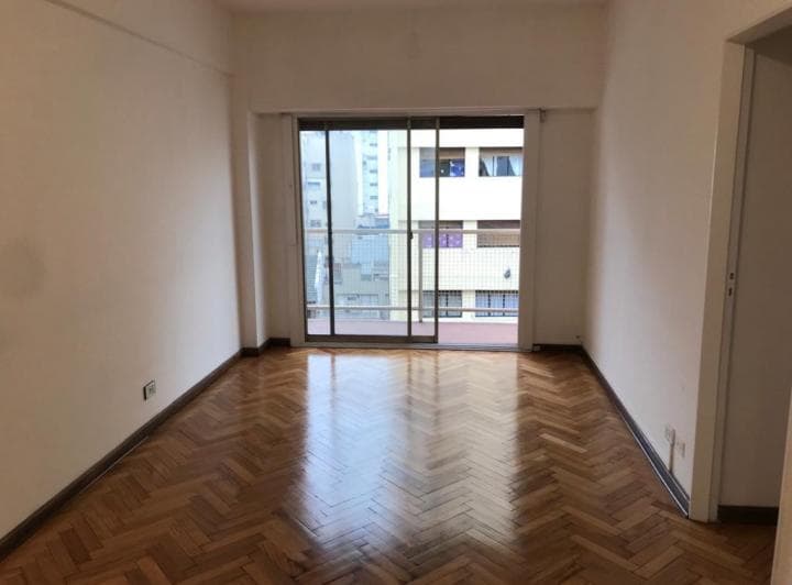 Living vacío con piso de parquet y un gran ventanal hacia el balcón.
