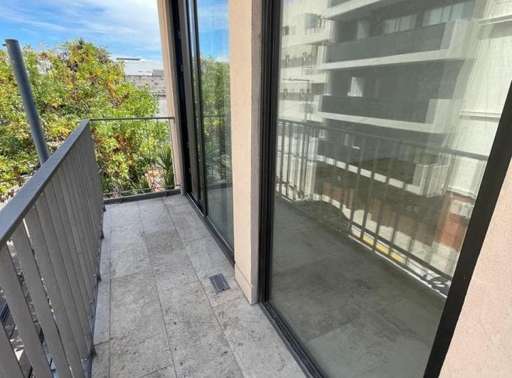 Balcón con baranda de metal, piso de mármol y vista a edificios y árboles.