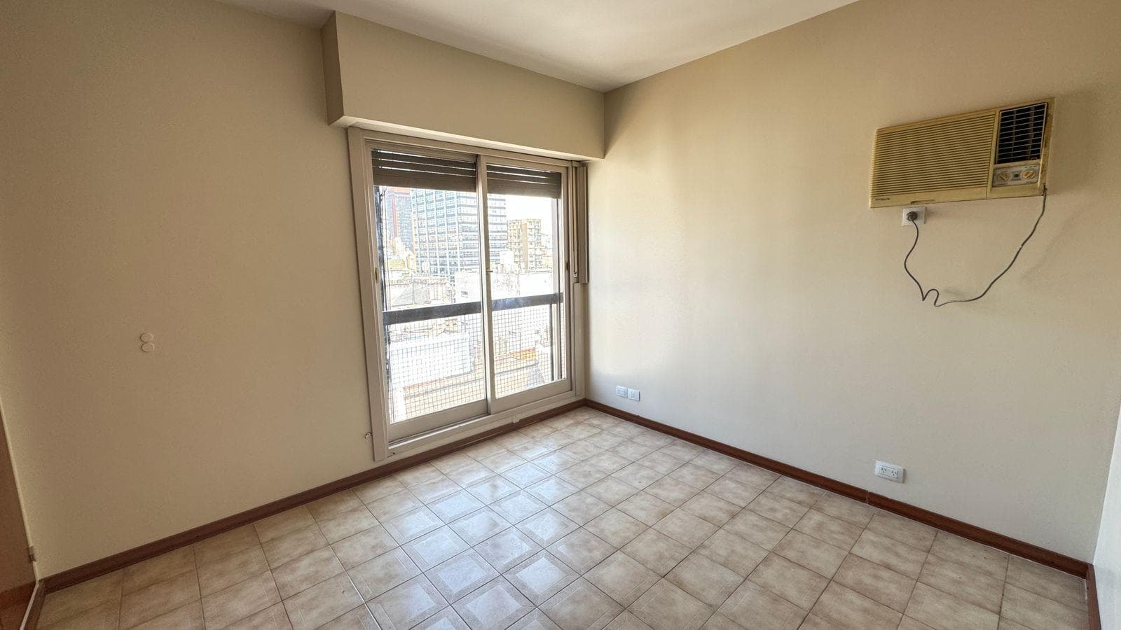 Living: ambiente vacío con piso de baldosas, ventana y aire acondicionado.