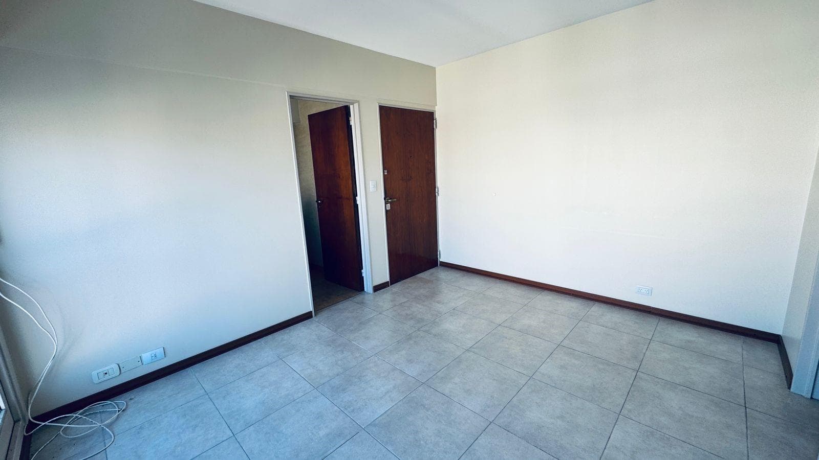 Living: ambiente vacío con piso de baldosas y dos puertas de madera.
