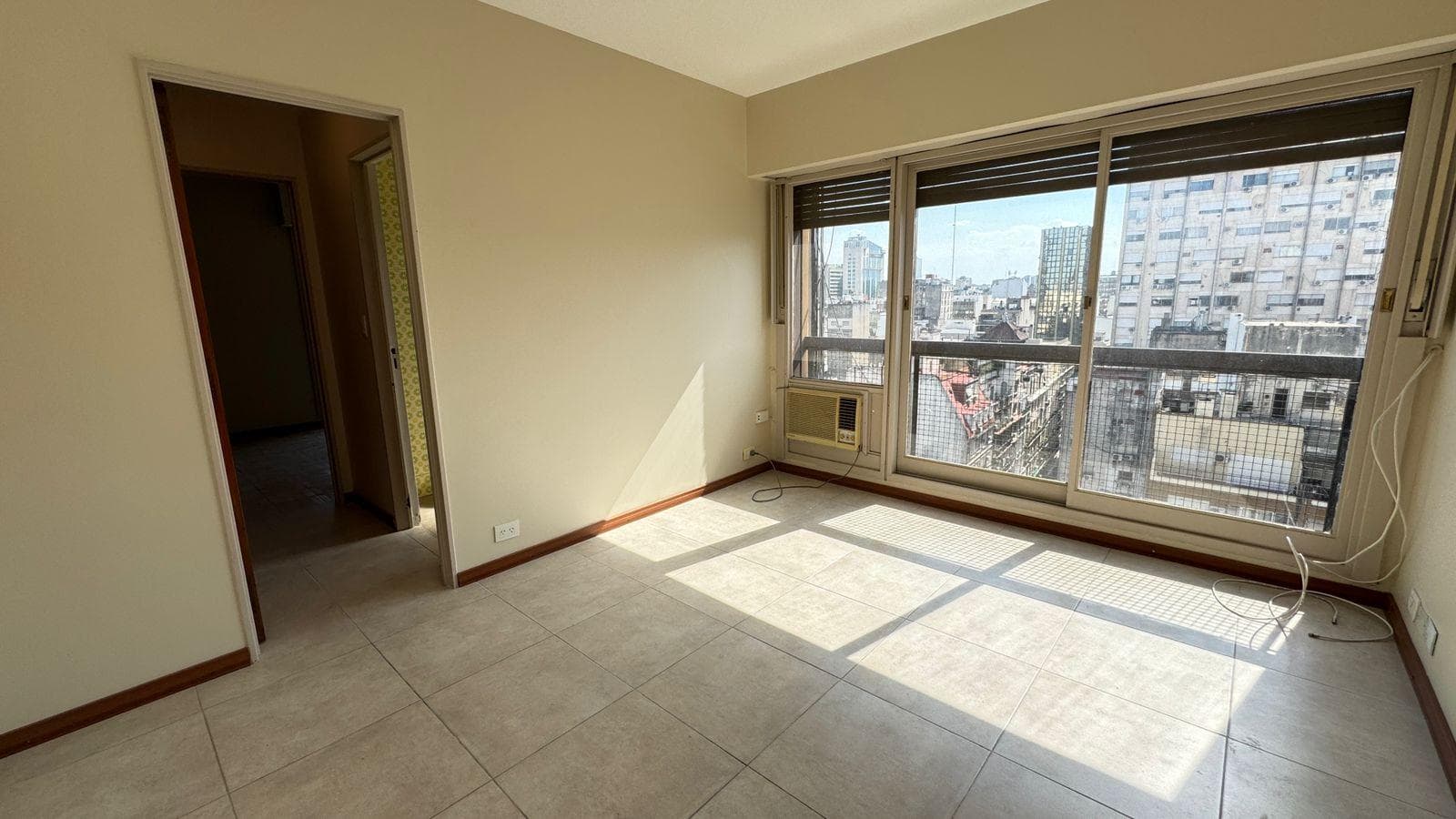 Living: ambiente vacío con ventana grande, piso de baldosas y aire acondicionado.