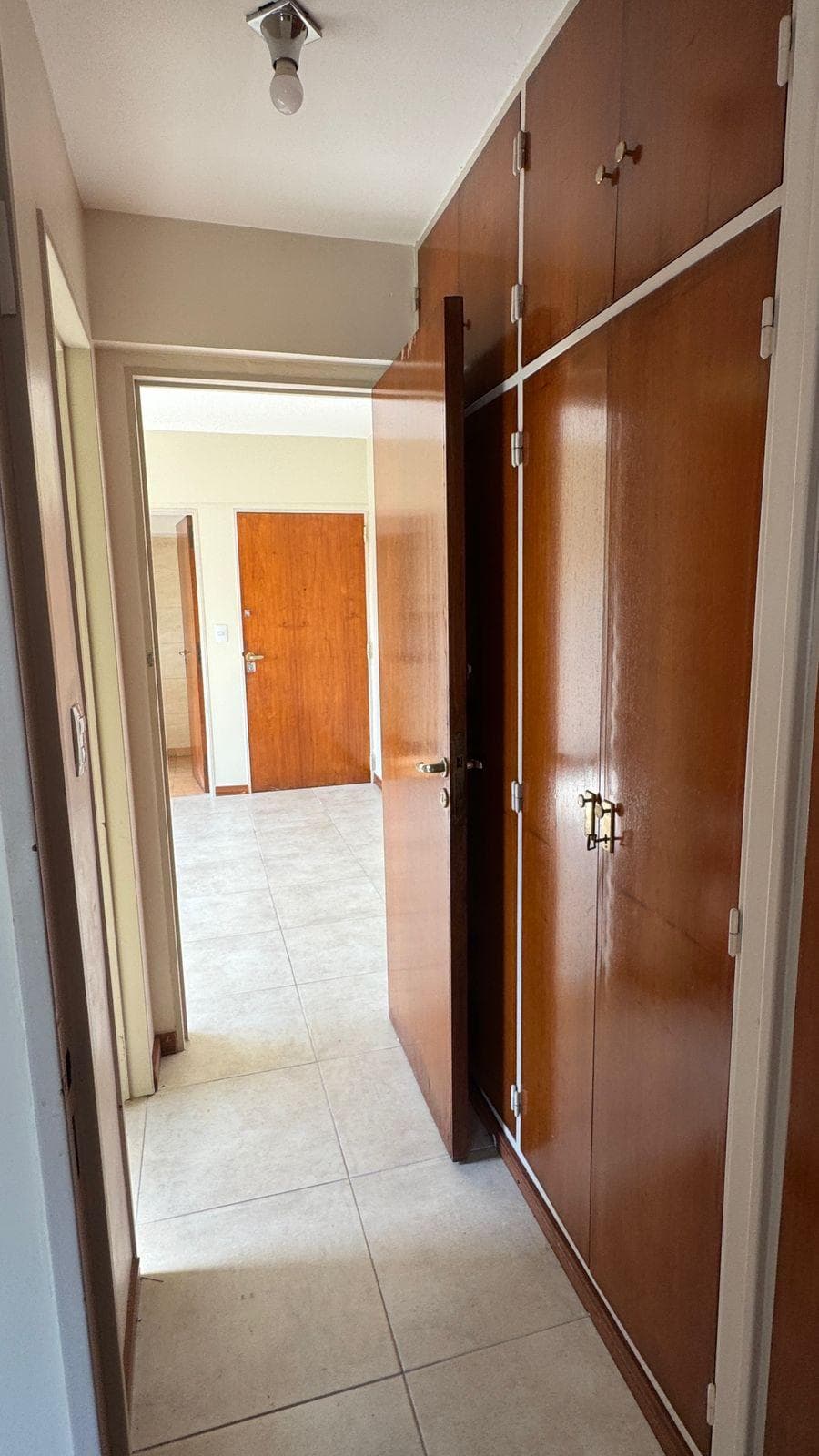 Pasillo: pasillo con placard de madera, puerta abierta y piso de baldosas.
