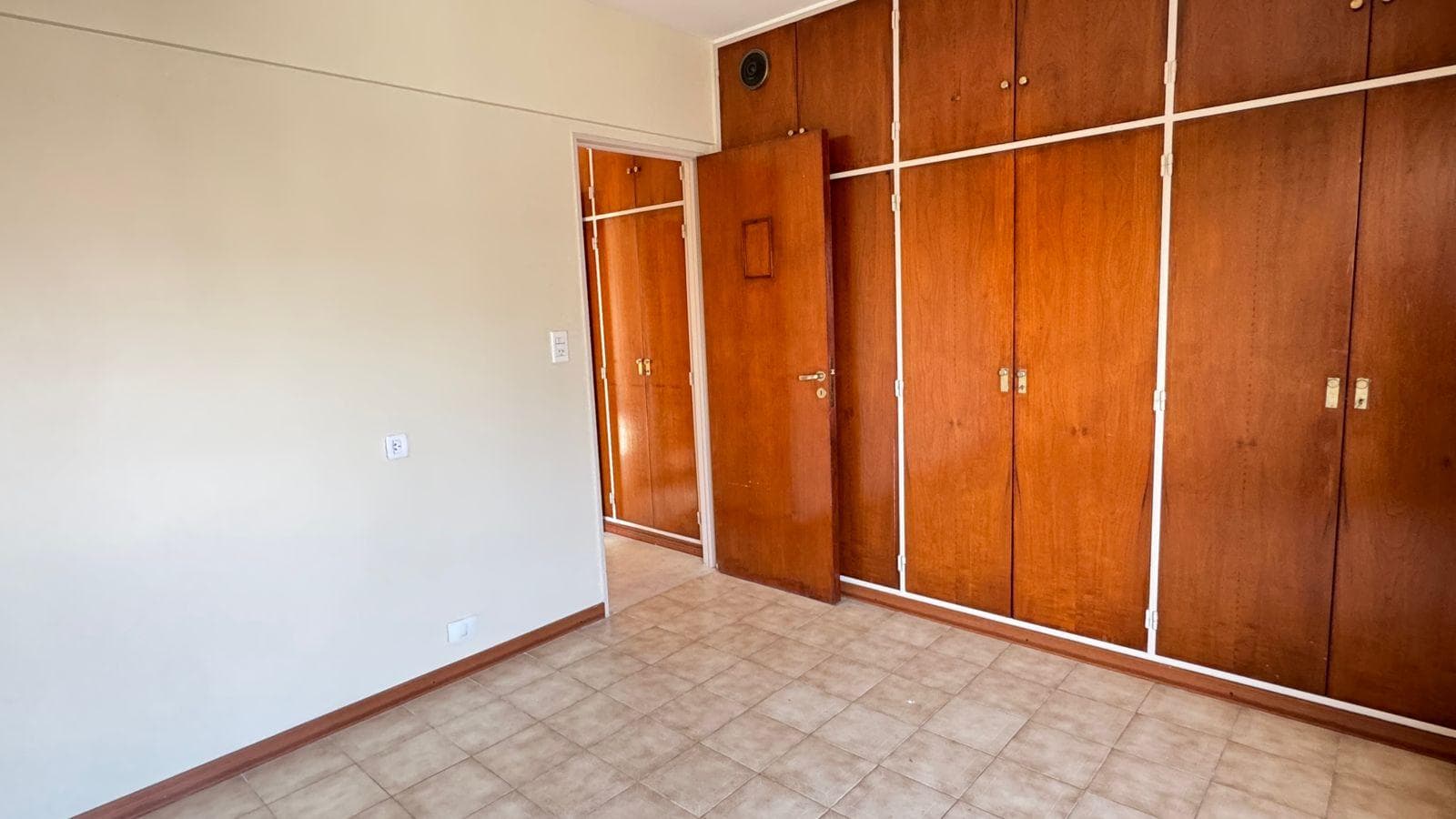 Dormitorio 1: cuarto vacío con placard de madera y piso de baldosas.